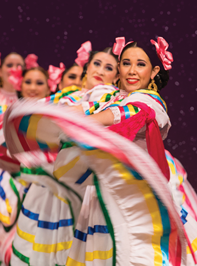 Image of women in colorful dresses dancing to mariachi music